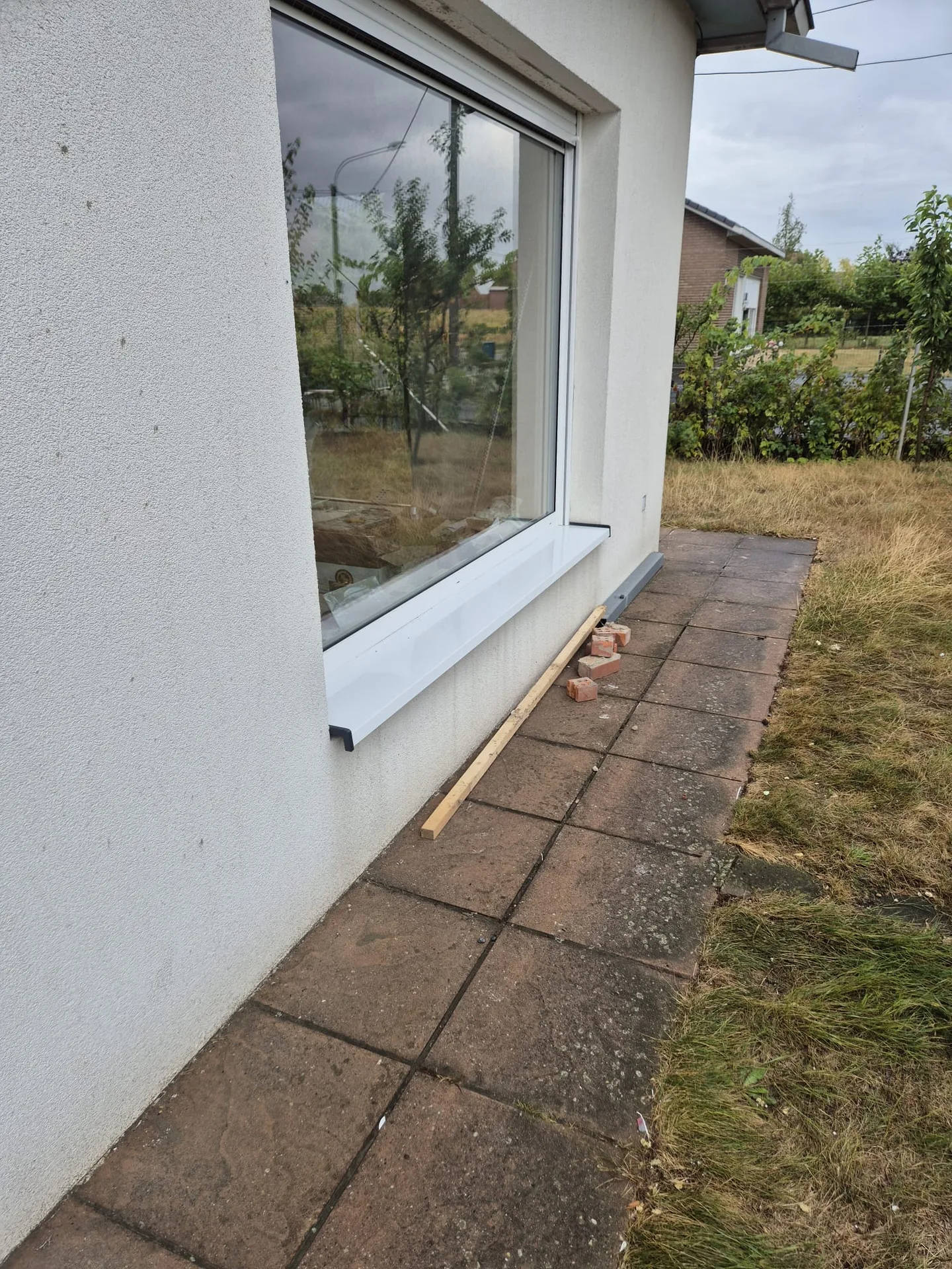 Groot PVC-raam met dubbele beglazing en witte buitenvensterbank in witgeverfd muurwerk