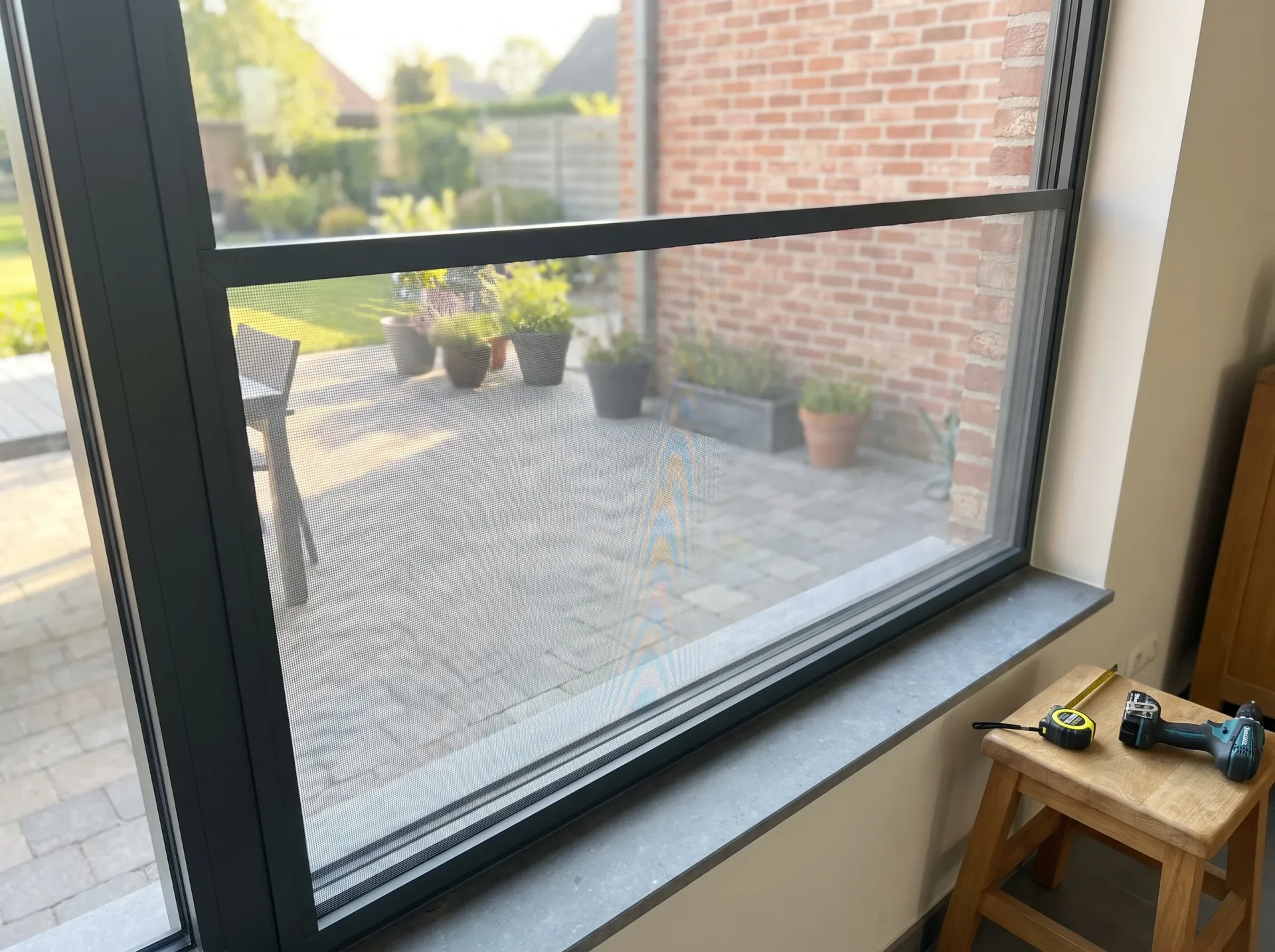 Insectenhorren op zwart raamkozijn, uitzicht op terras en tuin