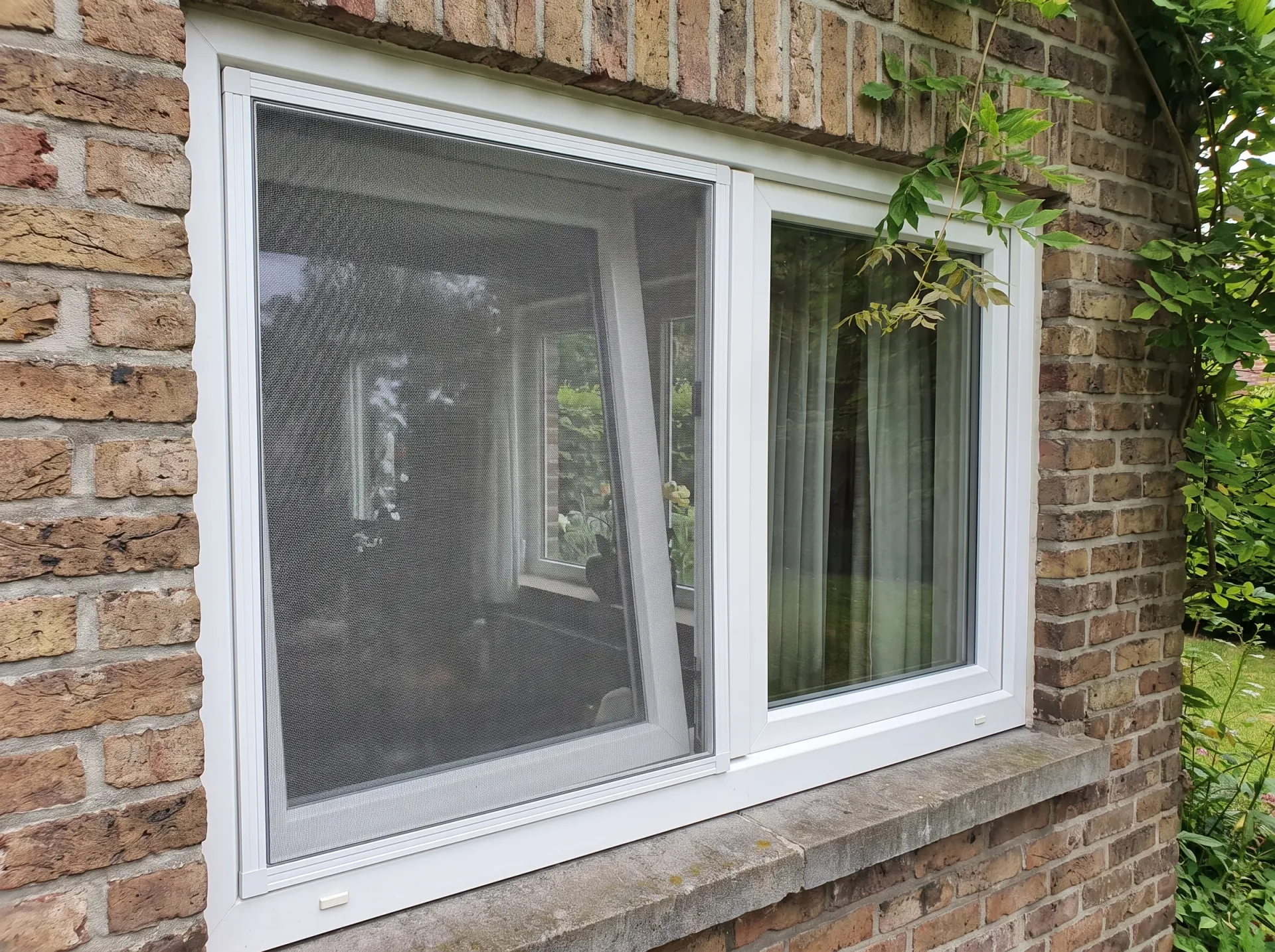 Geplaatste witte PVC-ramen met insectenhorren in bakstenen muur