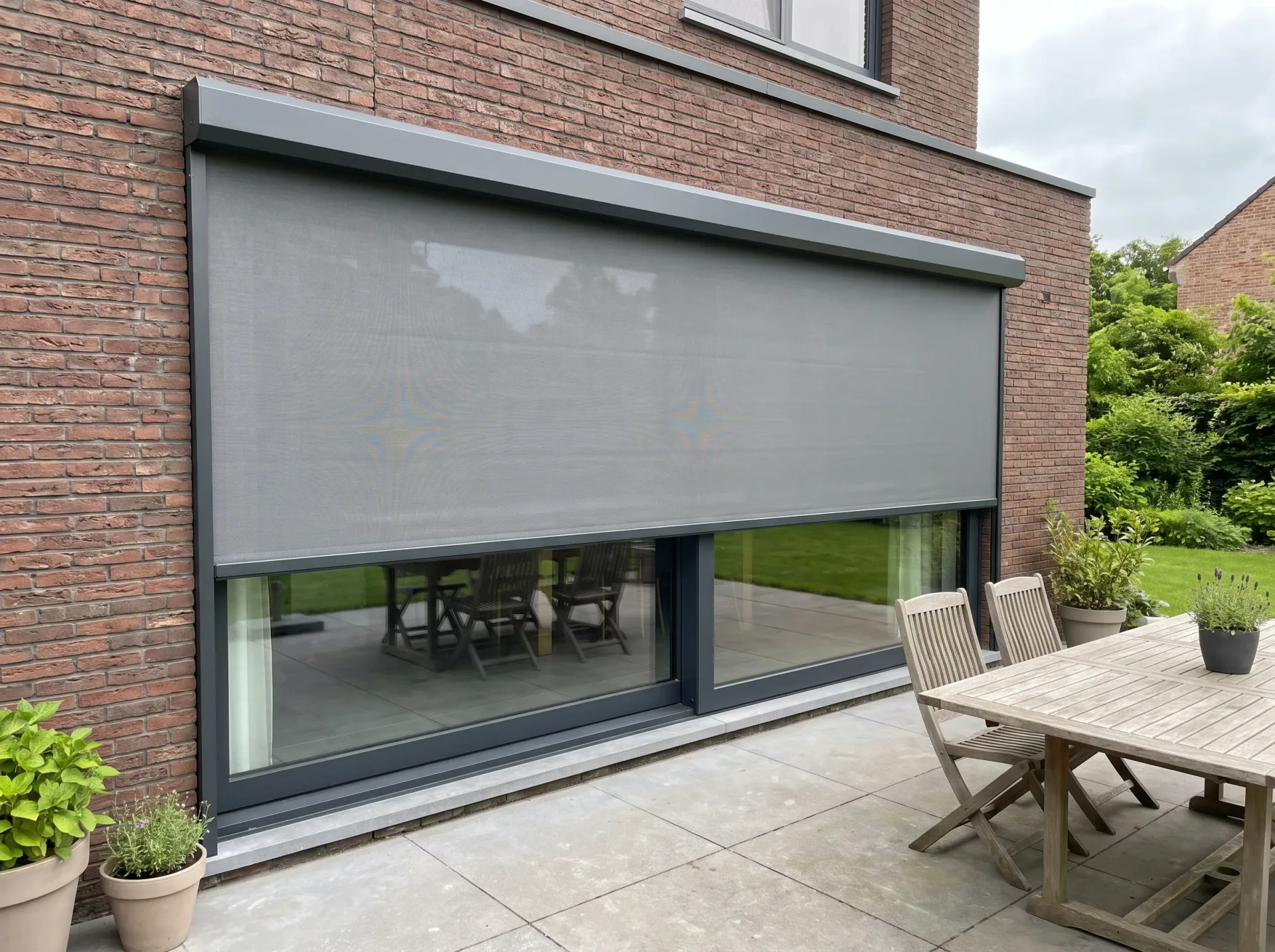 Aluminium schuifdeur met grijs buitenscreen op bakstenen gevel, uitzicht op terras en tuin